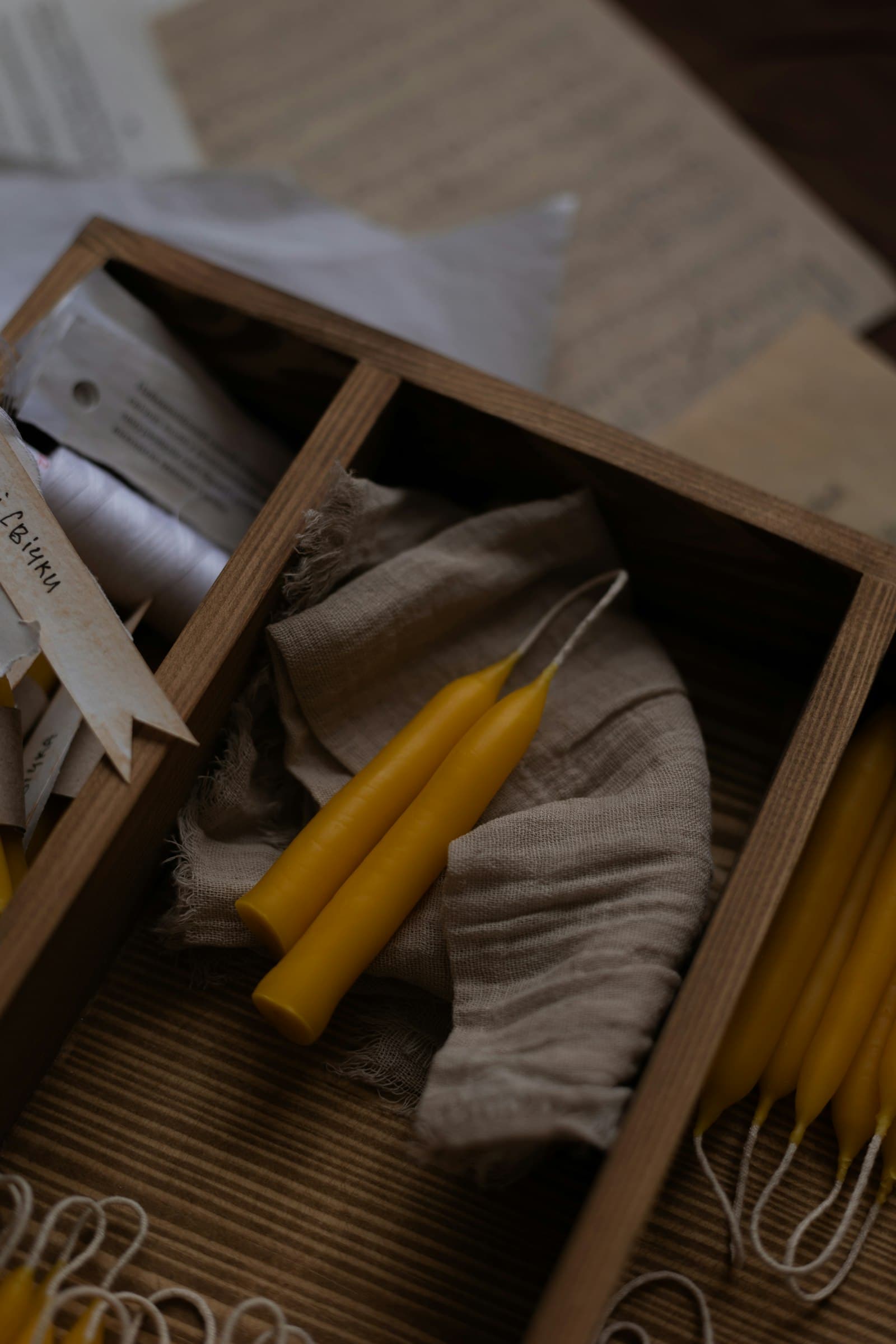 Unbleached beeswax tapers resting on linen in a compartmented wooden tray.