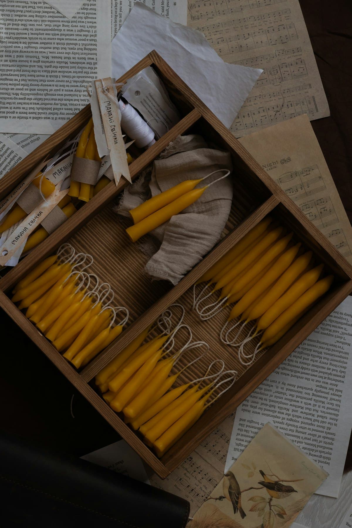 Finished beeswax tapers laid in a compartmented wooden tray with handwritten labels.