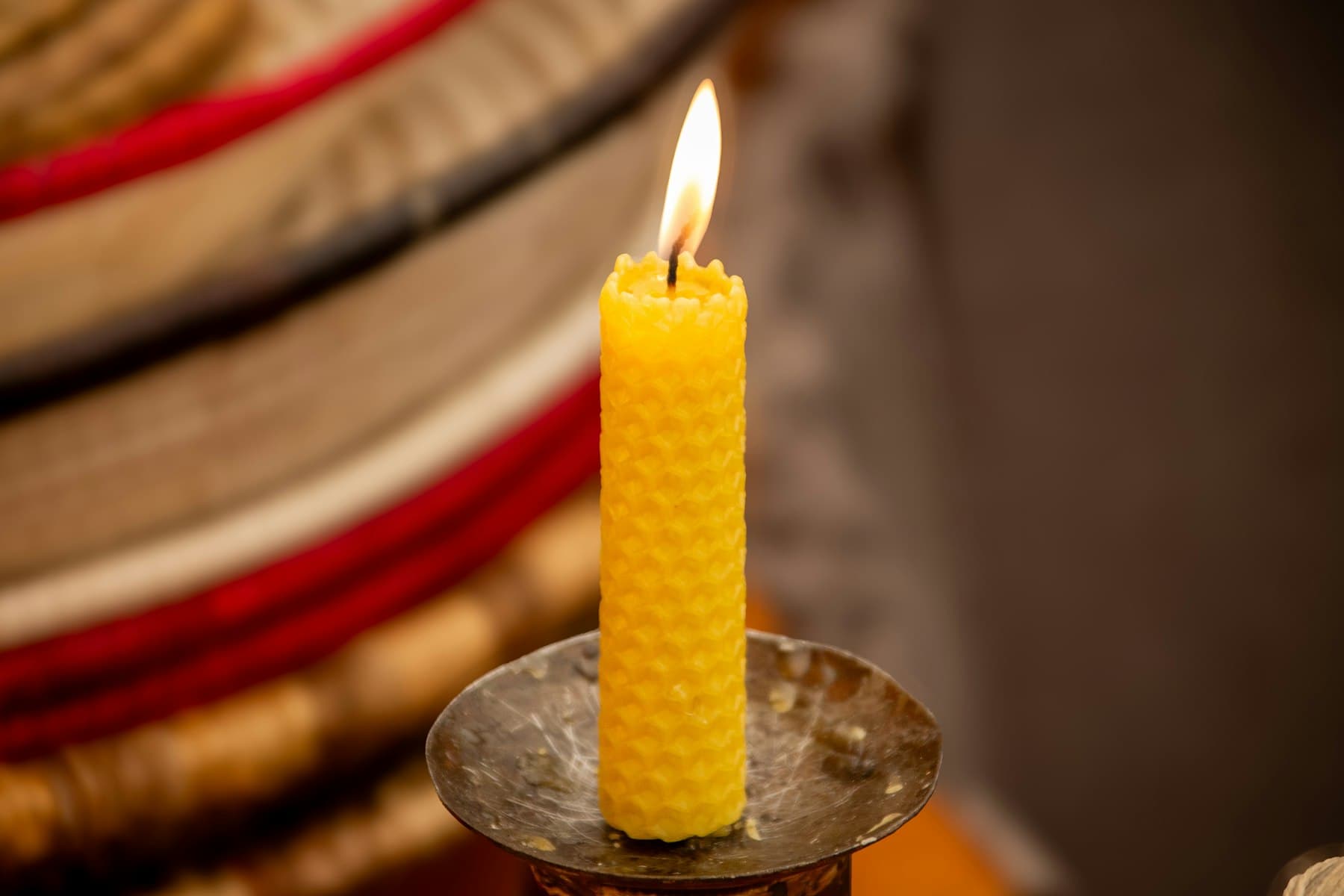 A single hand-rolled beeswax taper burning on a brass dish in a dim room.