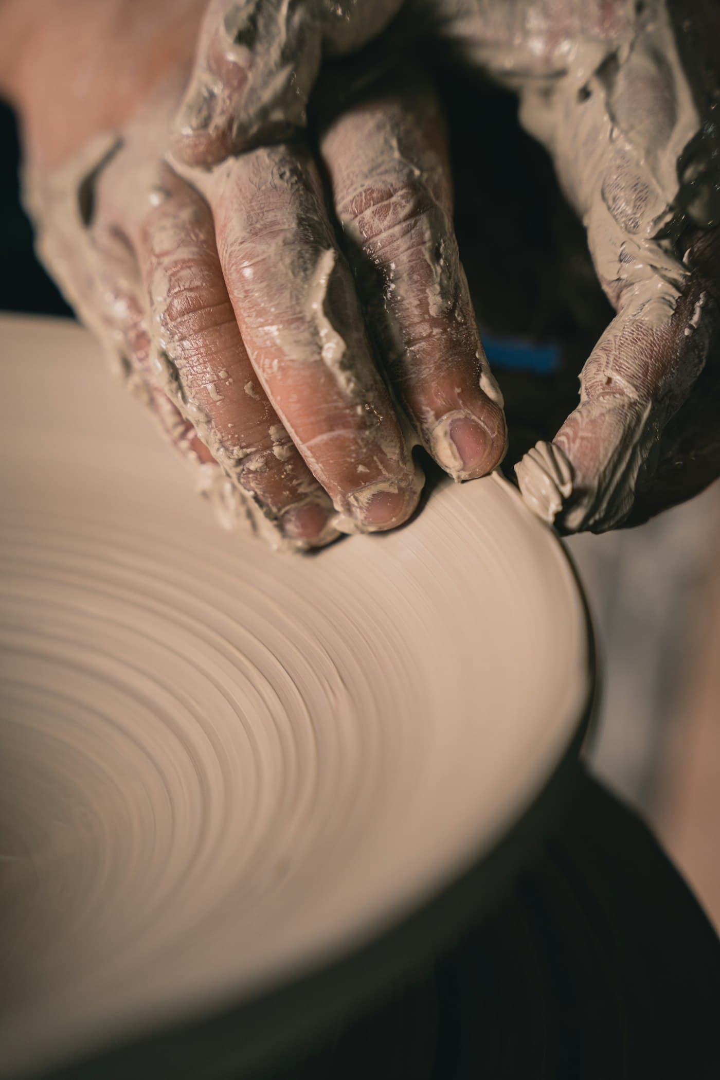 Clay-covered hands drawing up the wall of a vessel on a spinning wheel.