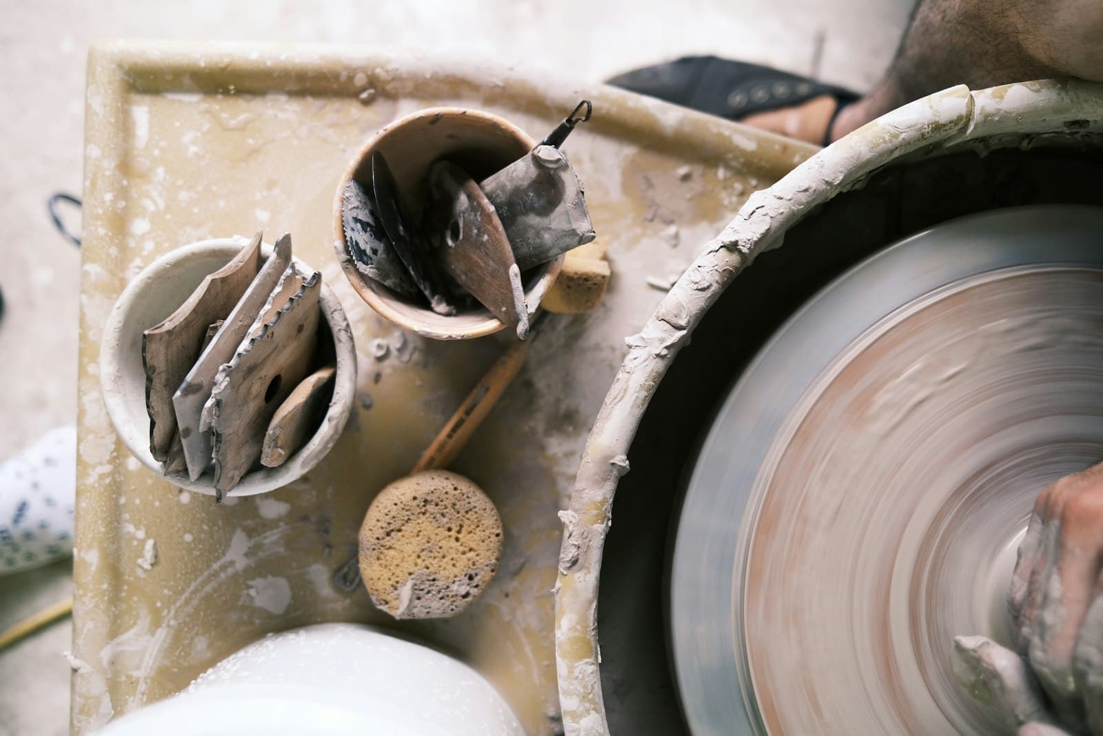 A working bench beside a potter’s wheel, crowded with ribs, sponges and half-finished clay forms.