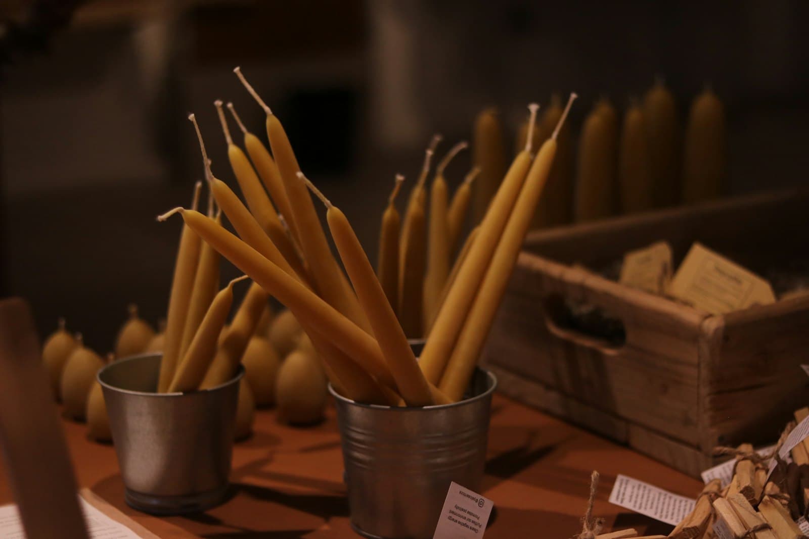 Slender beeswax tapers standing in copper cups on a workbench.