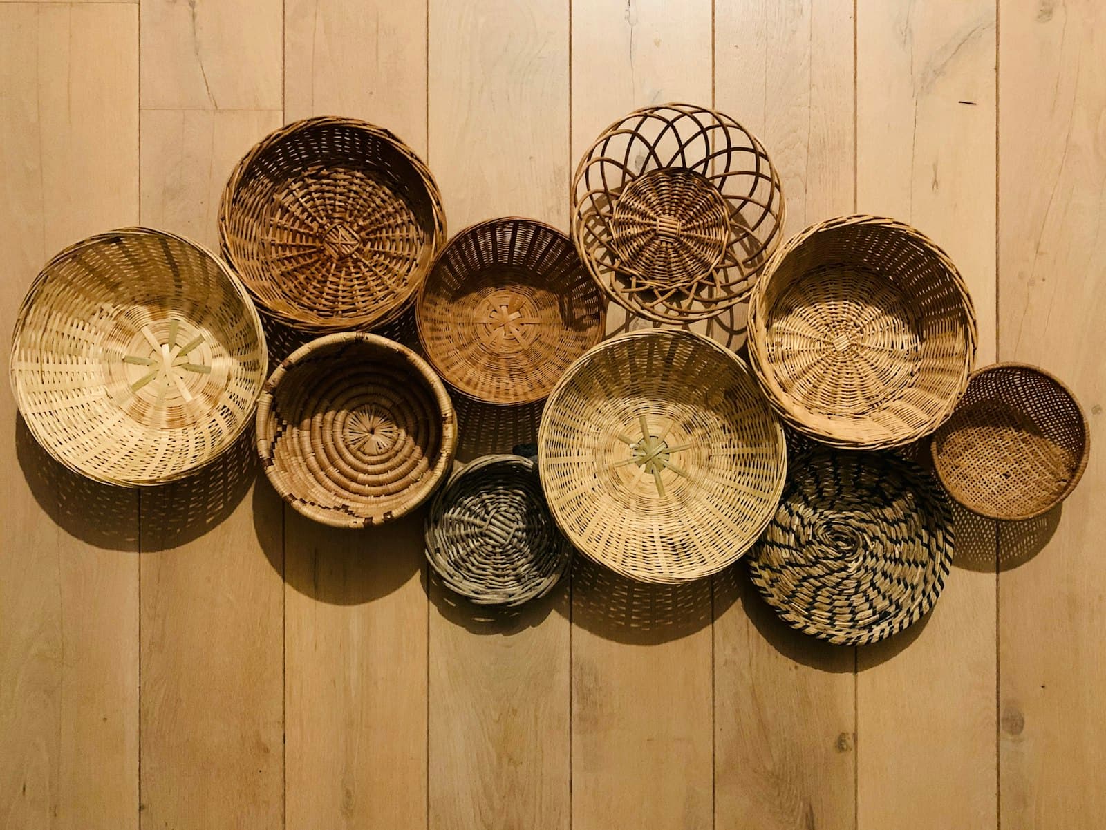 A group of shallow round woven trays arranged on a pale wooden floor.